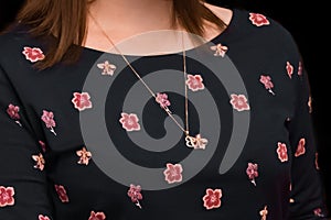 Women's neck jewelry pendant close-up on the background of a dark floral dress pattern