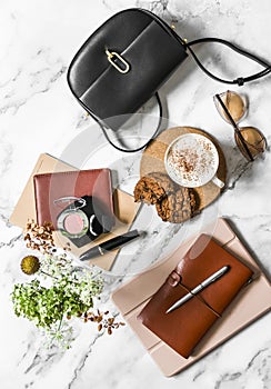 Women`s office desk - notebooks, organizer, tablet, cappuccino cup and cookies with chocolate drops on a marble background, top