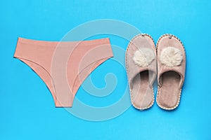 Women`s panties and warm slippers on a blue background. Minimal concept of women`s accessories