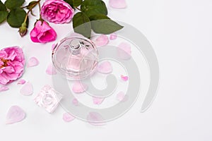 Women`s perfume in a glass bottle with pink flowers on a white background. empty space. Flat lay