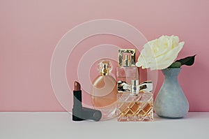 Women`s perfume, lipstick, white rose in a vase on the shelf. Minimalist interior.