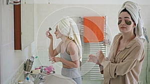 Women's secrets and gossip. Three young women with towels on their heads doing makeup while standing in front of a