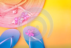 Women`s straw hat pink tropical flowers blue slippers sea shells on gradient duotone peachy yellow background. Beach vacation fash photo