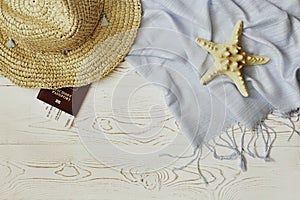 Women`s straw hat, red passport and plane ticket, blue tippet and starfish on a white wooden background - summer vacation concept