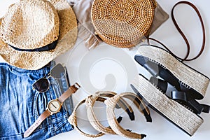 Women`s summer clothes collage on white, flat lay. Woven sandals, rattan bag, hat, watch, shorts, sunglasses top view