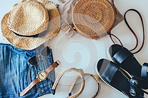 Women`s summer clothes collage on white, flat lay. Woven sandals, rattan bag, hat, watch, shorts, sunglasses top view