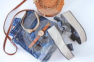 Women`s summer clothes collage on white, flat lay. Woven sandals, rattan bag, watch, shorts, sunglasses top view