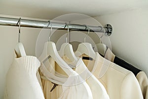 Women's sweaters and white shirts hang in the closet. Outdated clothes in the home wardrobe. Close-up