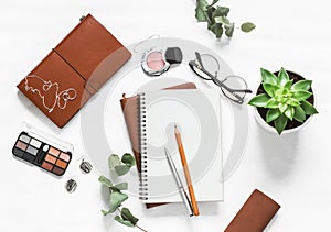 Women`s table with notebooks, make up cosmetic, pens, succulent flower on a light table, top view. Flat lay beauty female still