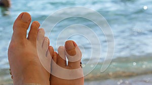 Women`s toes and feet against the background of the sea, the rays of the sun on the waves, beach vacation, summer resort