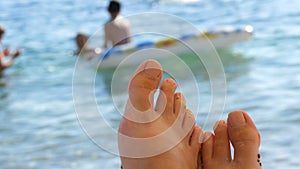 Women`s toes and feet against the background of the sea, the rays of the sun on the waves, beach vacation, summer resort
