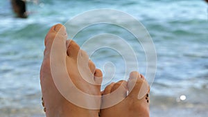 Women`s toes and feet against the background of the sea, the rays of the sun on the waves, beach vacation, summer resort