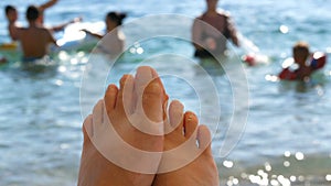 Women`s toes and feet against the background of the sea, the rays of the sun on the waves, beach vacation, summer resort