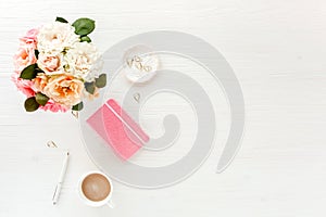 Women`s workspace with pink and beige roses flowers, accessories, diary on white background. Flat lay, top view trendy