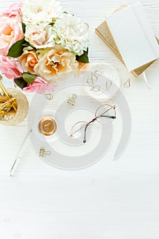 Women`s workspace with pink and beige roses flowers bouquet, accessories, diary, glasses on white background. Flat lay