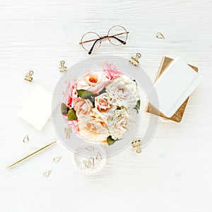 Women`s workspace with pink and beige roses flowers bouquet, accessories, diary, glasses on white background. Flat lay