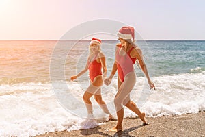 Women in Santa Claus hats run into the sea dressed in red swimsuits. Celebrating the New Year in a hot country