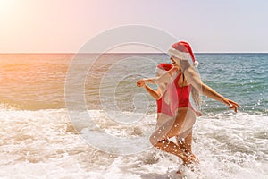 Women in Santa Claus hats run into the sea dressed in red swimsuits. Celebrating the New Year in a hot country