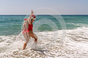 Women in Santa Claus hats run into the sea dressed in red swimsuits. Celebrating the New Year in a hot country