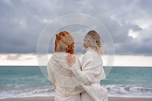 Women sea walk friendship spring. Two girlfriends, redhead and blonde, middle-aged walk along the sandy beach of the sea