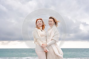 Women sea walk friendship spring. Two girlfriends, redhead and blonde, middle-aged walk along the sandy beach of the sea