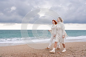 Women sea walk friendship spring. Two girlfriends, redhead and blonde, middle-aged walk along the sandy beach of the sea