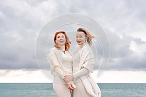 Women sea walk friendship spring. Two girlfriends, redhead and blonde, middle-aged walk along the sandy beach of the sea