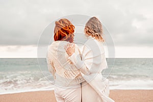 Women sea walk friendship spring. Two girlfriends, redhead and blonde, middle-aged walk along the sandy beach of the sea