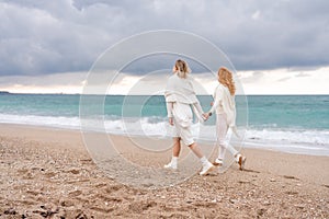 Women sea walk friendship spring. Two girlfriends, redhead and blonde, middle-aged walk along the sandy beach of the sea