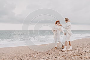 Women sea walk friendship spring. Two girlfriends, redhead and blonde, middle-aged walk along the sandy beach of the sea