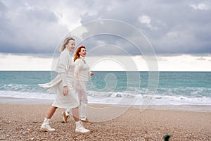 Women sea walk friendship spring. Two girlfriends, redhead and blonde, middle-aged walk along the sandy beach of the sea