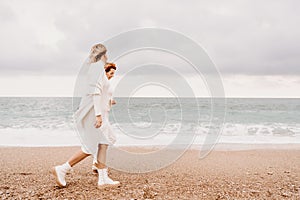 Women sea walk friendship spring. Two girlfriends, redhead and blonde, middle-aged walk along the sandy beach of the sea
