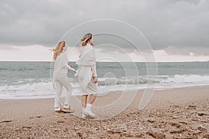 Women sea walk friendship spring. Two girlfriends, redhead and blonde, middle-aged walk along the sandy beach of the sea