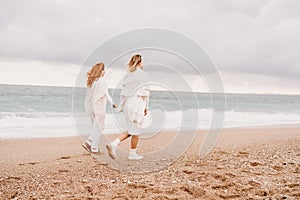 Women sea walk friendship spring. Two girlfriends, redhead and blonde, middle-aged walk along the sandy beach of the sea