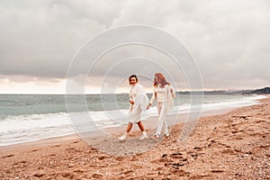 Women sea walk friendship spring. Two girlfriends, redhead and blonde, middle-aged walk along the sandy beach of the sea