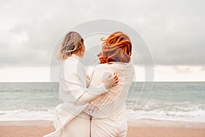 Women sea walk friendship spring. Two girlfriends, redhead and blonde, middle-aged walk along the sandy beach of the sea