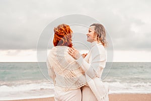 Women sea walk friendship spring. Two girlfriends, redhead and blonde, middle-aged walk along the sandy beach of the sea