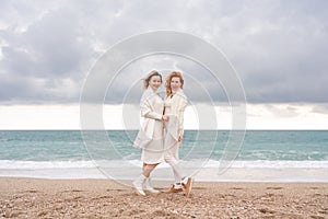 Women sea walk friendship spring. Two girlfriends, redhead and blonde, middle-aged walk along the sandy beach of the sea