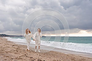 Women sea walk friendship spring. Two girlfriends, redhead and blonde, middle-aged walk along the sandy beach of the sea