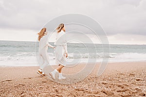 Women sea walk friendship spring. Two girlfriends, redhead and blonde, middle-aged walk along the sandy beach of the sea