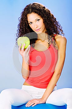 Women seating on blue pilates ball holding green apple