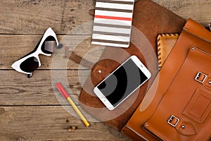 women set with bag, smart phone, sunglasses, notepad, pen and purse on brown wooden desk