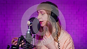 Women singer in recording studio sings song into microphone with pop filter