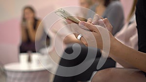 Women sit at a conference with phones. Women write down information to themselves in phone. typing text on touch screen