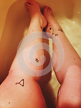 Women sitting in a low water bath with black ink tattoos covering her legs