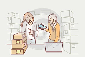 Women small business owners making fulfillment startup stands among cardboard boxes and uses laptop