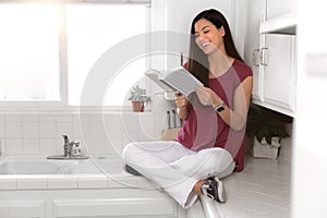 Women smiling laughing and deep into book, sitting on kitchen counter, alone, enjoying free time