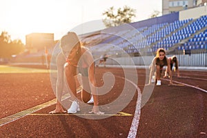 Women sprinters at starting position ready for race on racetrack.