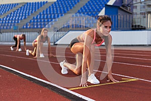 Women sprinters at starting position ready for race on racetrack.