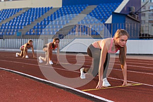 Women sprinters at starting position ready for race on racetrack.